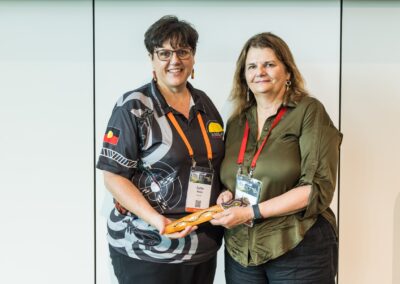 Kellie Kerin and Linda Kensington holding Message Stick - a col­lec­tive mes­sage of Cul­tur­al Safe­ty, craft­ed by the group, was then tak­en for­ward and passed on to the wider conference.