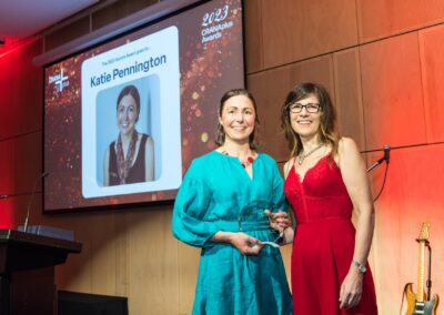 Katie Pennington stood on stage holding her 2023 Aurora Award trophy.