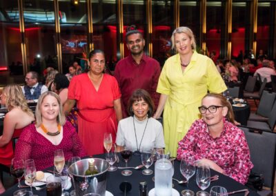 Group of people sat around a circle dinner table, smiling.