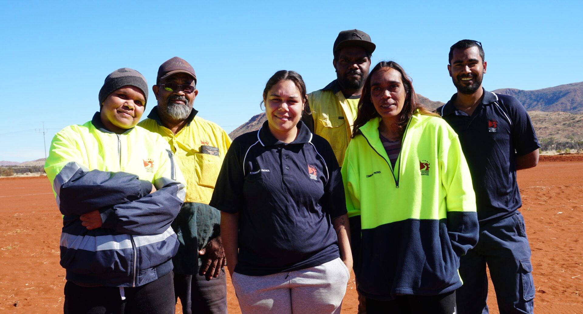 Group of people stood on red soil, smiling