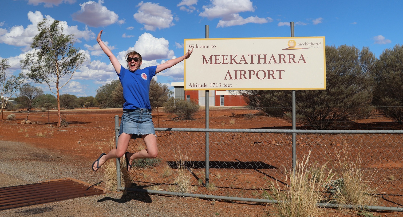 Sarah jumping for joy in front of Meekatharra Airport sign