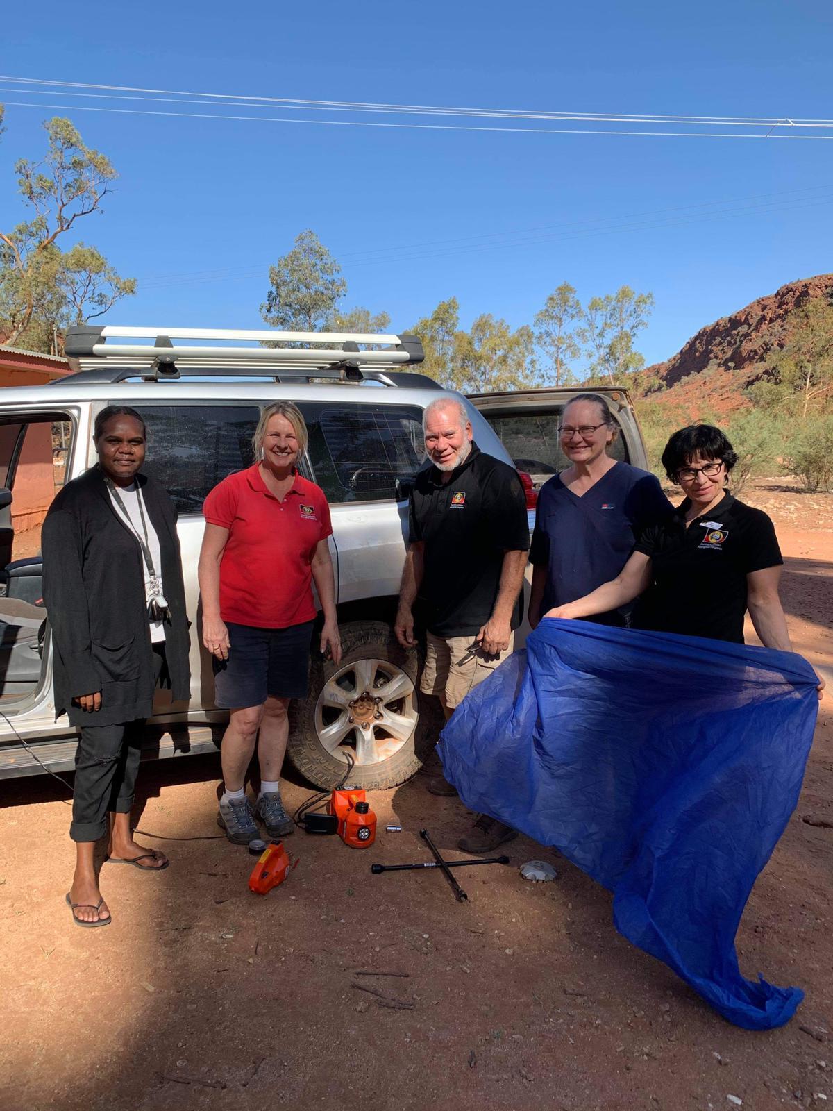 Utju-team-Gayle-Woodford-Article.jpg Group of people standing in front of care, one is holding a blue tarp