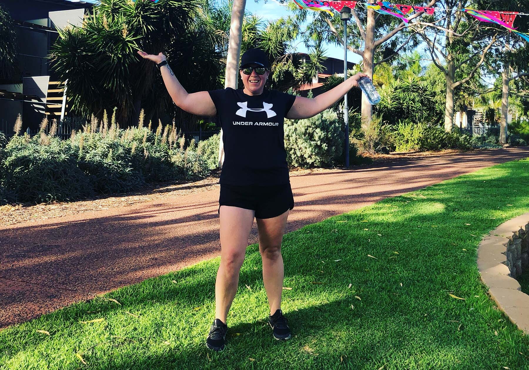 Kelly in activewear, holding arms up and smiling.